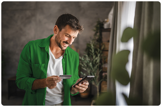 Jonge man met zijn telefoon in zijn hand die een overschrijving doet met zijn bankkaart