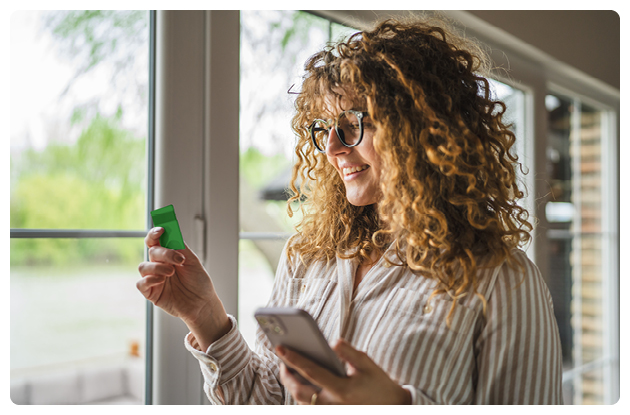 Woman with glasses looking happy at her card while holding smartphone